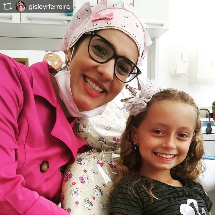 Dra. Anne e uma paciente com laço no cabelo, sorrindo lado a lado.