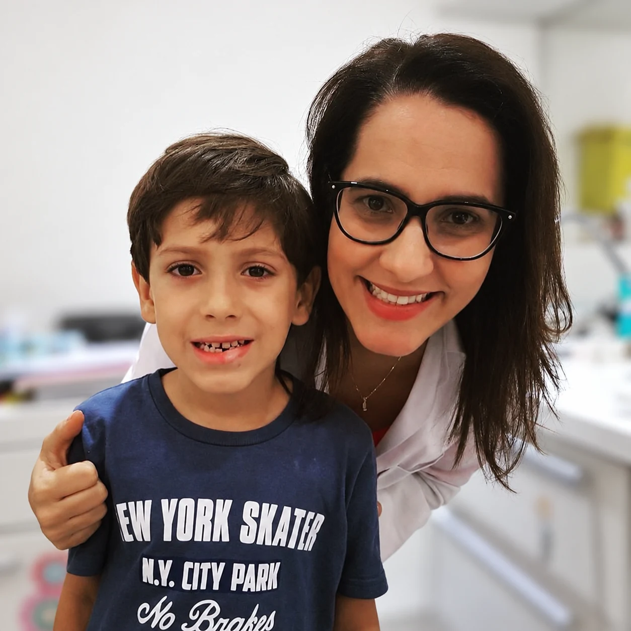 Dra. Anne abraçada a um menino, os dois sorrindo no consultório.