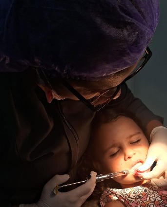Dra. Anne atendendo com cuidado uma menina tranquila, de olhos fechados, na cadeira do consultório.