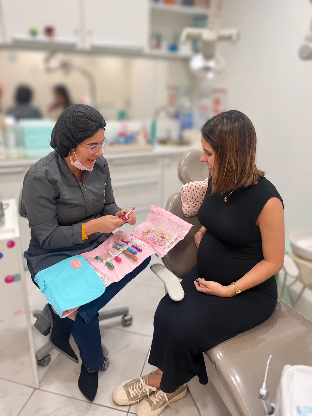 Dra. Anne conversando com uma gestante e mostrando materiais de cuidado bucal.